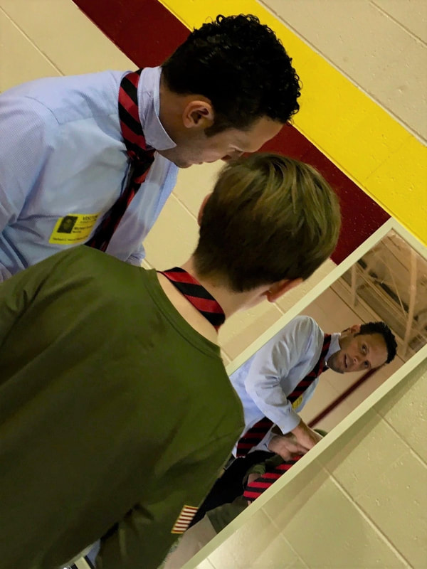 Michael Ayers helping a young boy tie his tie in the mirror